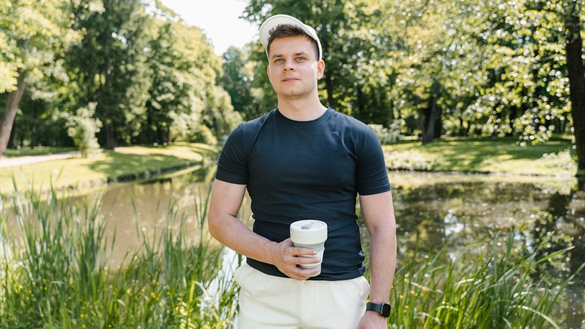 Casual young man in a park, holding a coffee cup. Sunny day in nature.