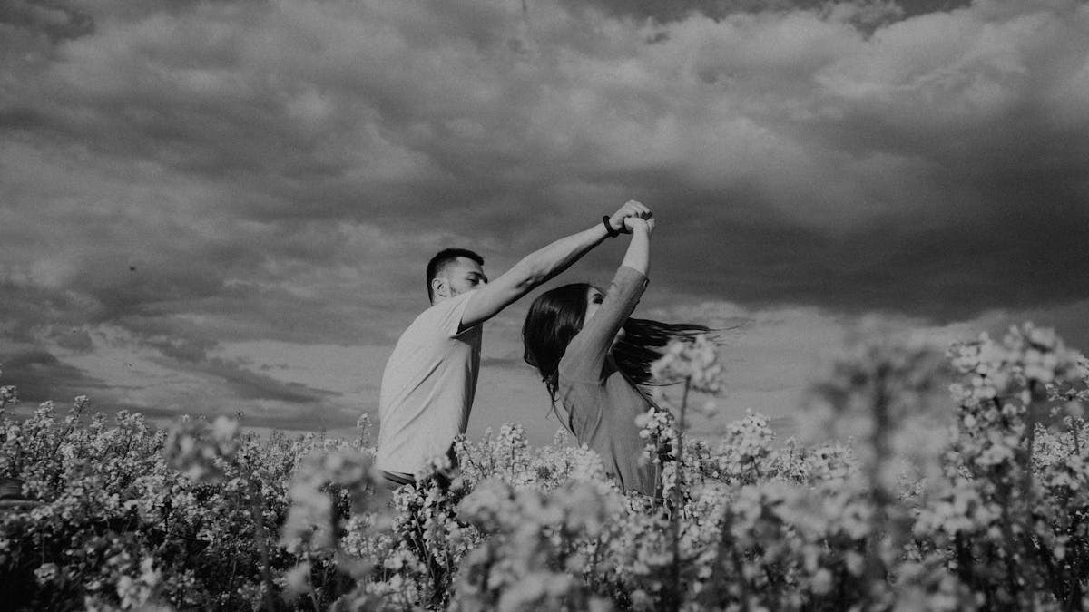 A romantic couple dances in a blooming flower field under dramatic skies in black and white.